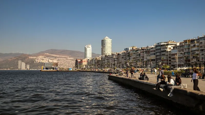 Kordon'da deniz kıyısında yürüyen insanlar ve arkada yüksek apartman blokları