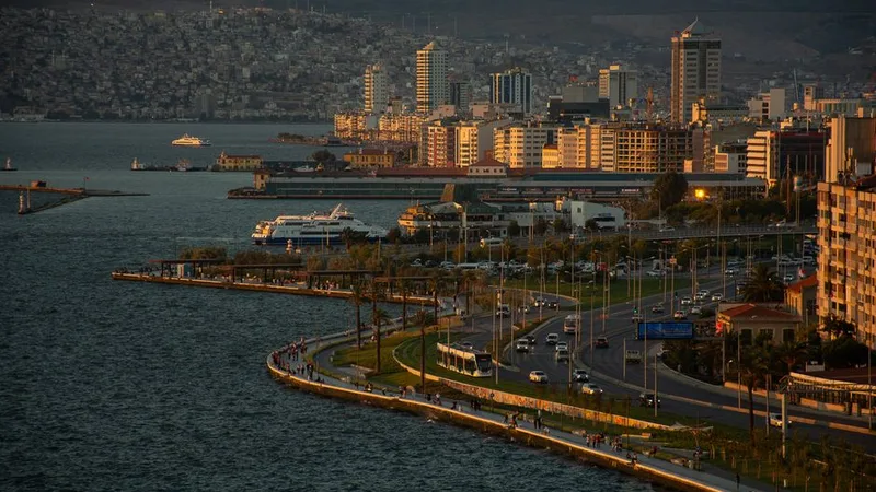 Gün batımında İzmir Kordon'u, palmiye ağaçları ve tramvay hattı ile şehir manzarası