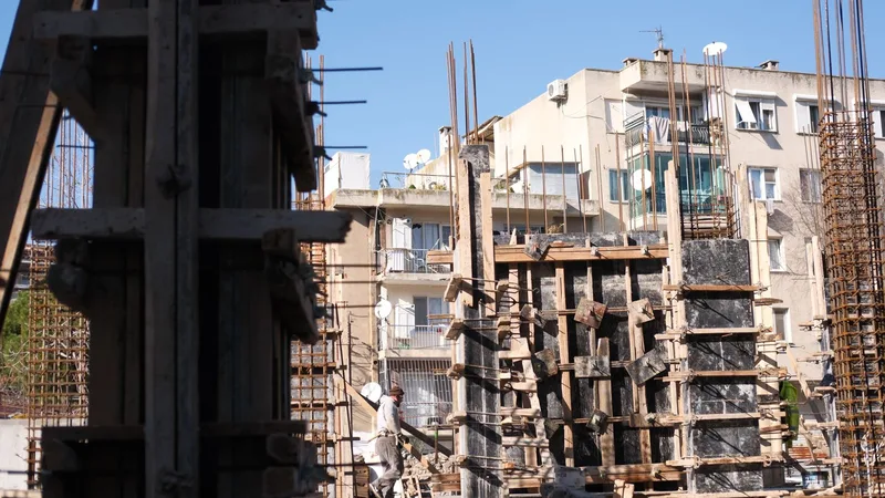 Yükselen bir bina inşaatının önünde, balkonlu ve uydu antenli eski bir apartman