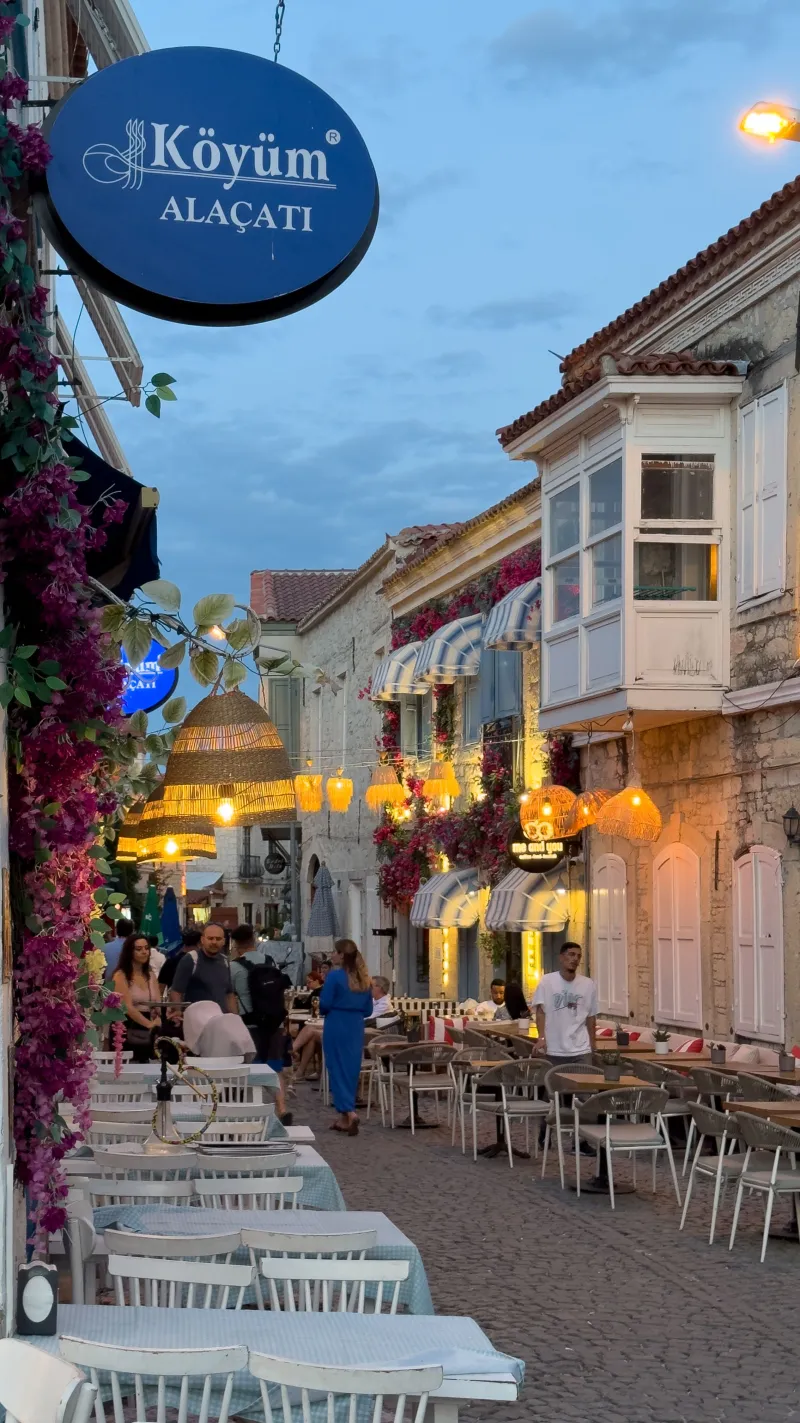 Akşam ışıklarıyla aydınlanmış, taş cepheli dar bir Alaçatı sokağı