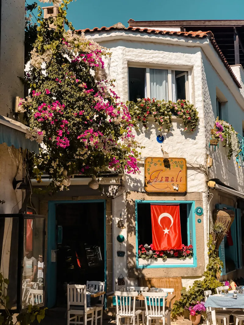 Bugenvil çiçekleriyle kaplı, Türk bayraklı bir Alaçatı restoranı cephesi