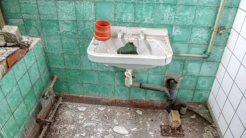 Eski, çatlamış fayansları ve paslı borularıyla yenilemeyi bekleyen bir banyo