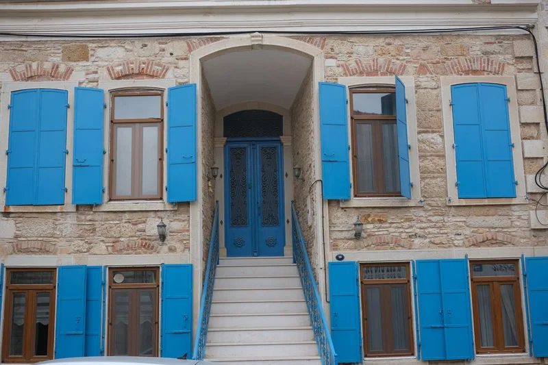 Mavi kepenkli pencereleri olan eski bir taş ev cephesi