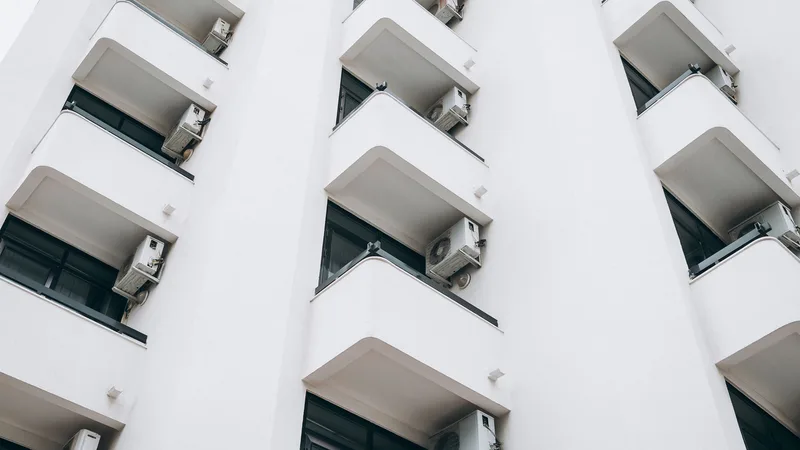 Beyaz bir apartmanın balkonlarına monte edilmiş klima dış ünitelerinin alttan görünümü