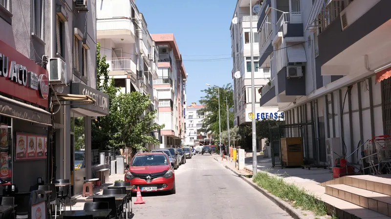Dar bir sokakta park etmiş kırmızı bir araba, iki yanında apartmanlar