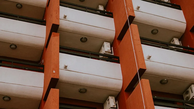 Turuncu sütunlu bir apartmanın balkon altlarından yakın çekim, klima üniteleri görünüyor