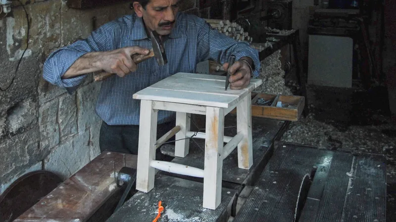 Ahşap bir tabure üzerinde el aletleriyle çalışan bir marangoz