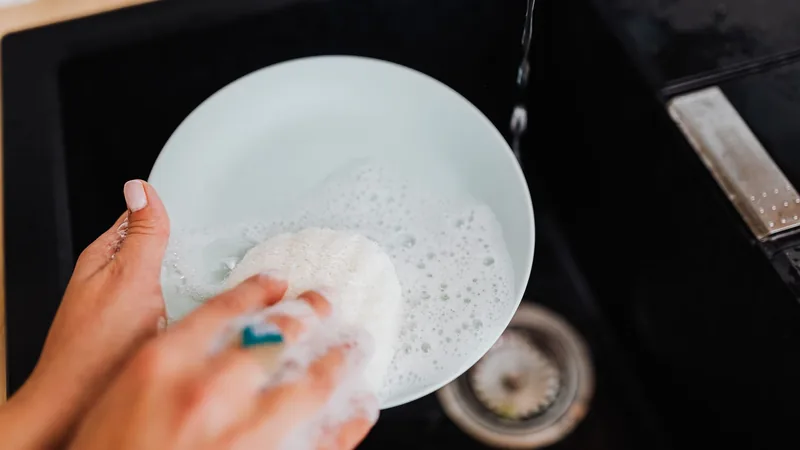 Bulaşık yıkayan bir el, köpüklü tabak ve lavabo